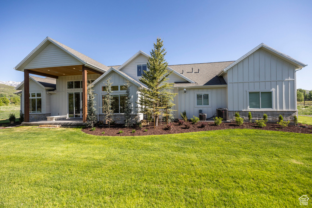 Rear view of house featuring board and batten siding, a shingled roof, and a lawn