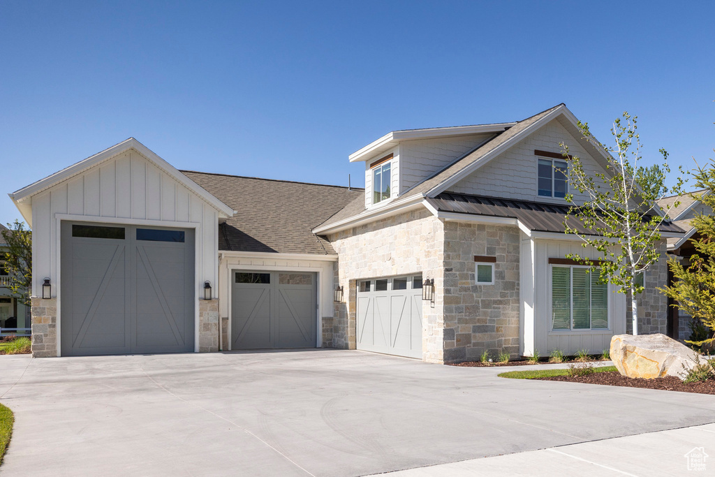 View of front of property featuring stone siding, concrete driveway, a garage, board and batten siding, and roof with shingles