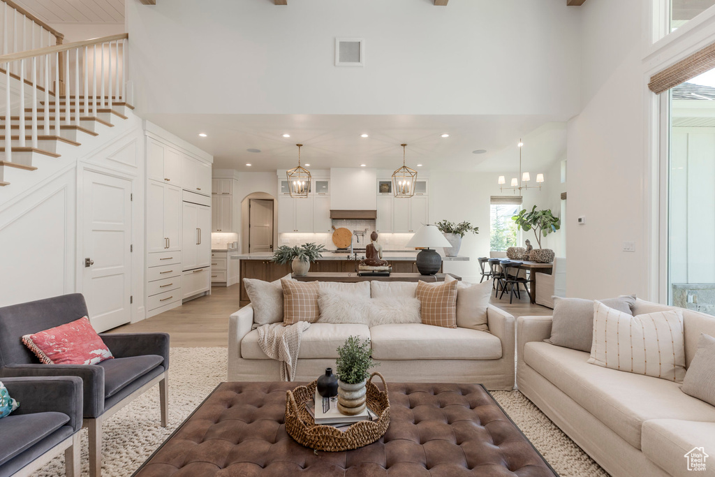 Living area with a chandelier, a towering ceiling, light wood finished floors, recessed lighting, and arched walkways