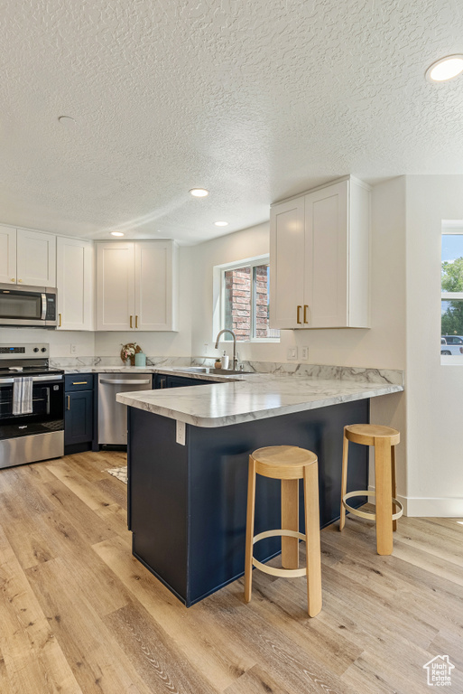Kitchen featuring stainless steel appliances, white cabinetry, a textured ceiling, a peninsula, and a sink