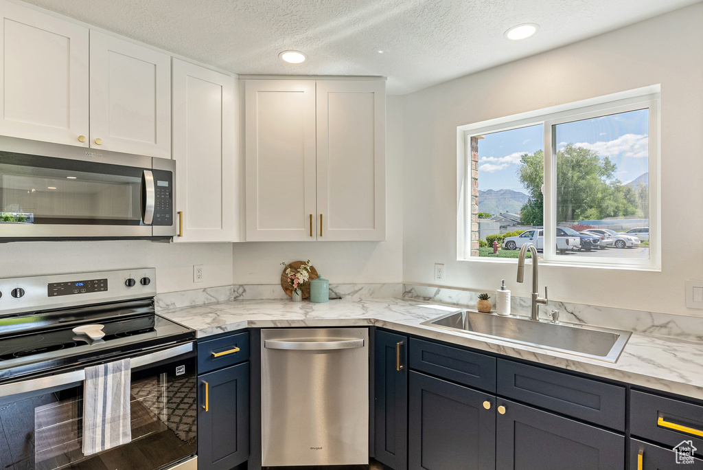 Kitchen with appliances with stainless steel finishes, a sink, white cabinets, a textured ceiling, and recessed lighting