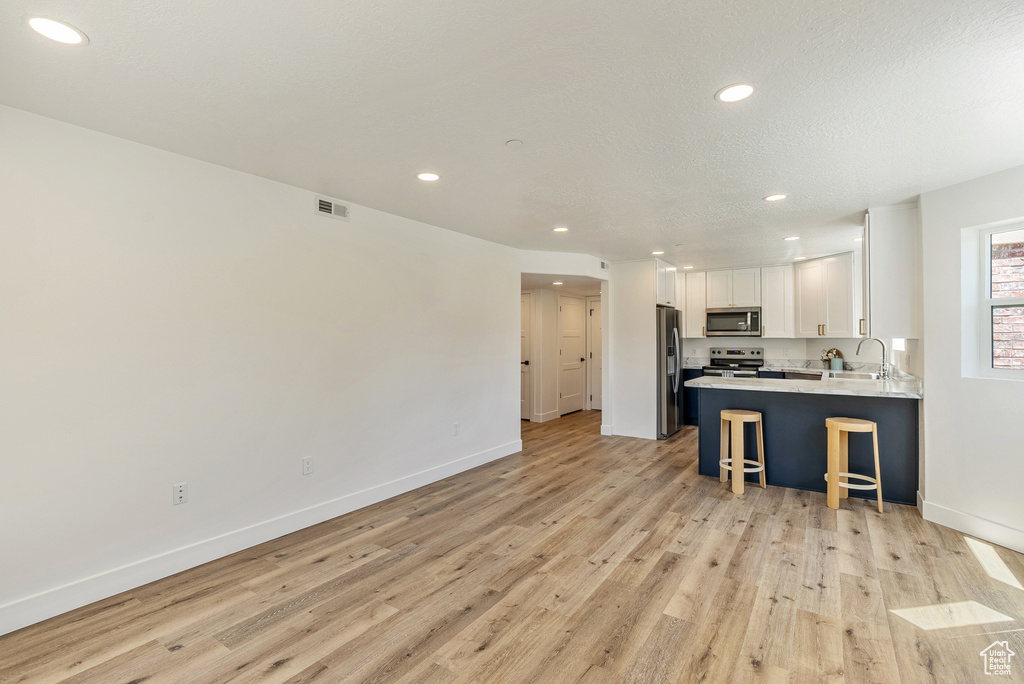 Kitchen featuring stainless steel appliances, light wood-style flooring, a kitchen bar, white cabinetry, and recessed lighting