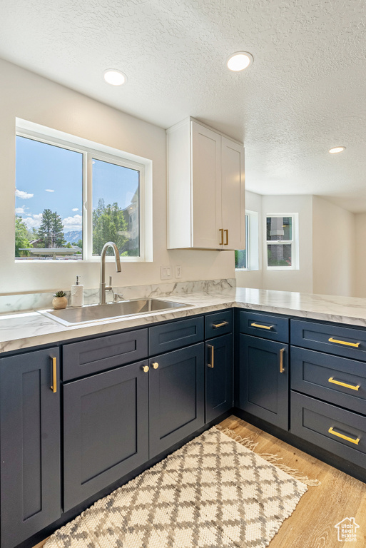 Kitchen featuring a sink, white cabinets, light wood finished floors, light countertops, and a textured ceiling
