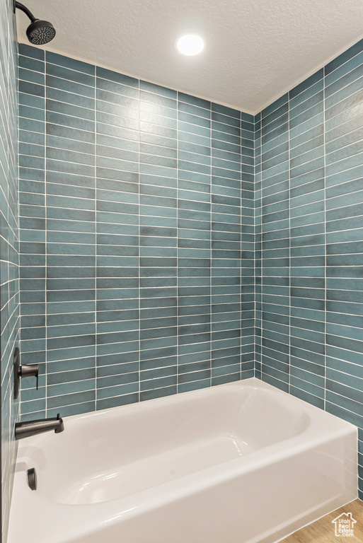 Bathroom featuring a textured ceiling,  shower combination, and tile walls