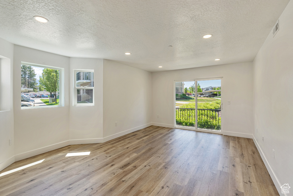 Empty room with healthy amount of natural light, a textured ceiling, wood finished floors, baseboards, and recessed lighting