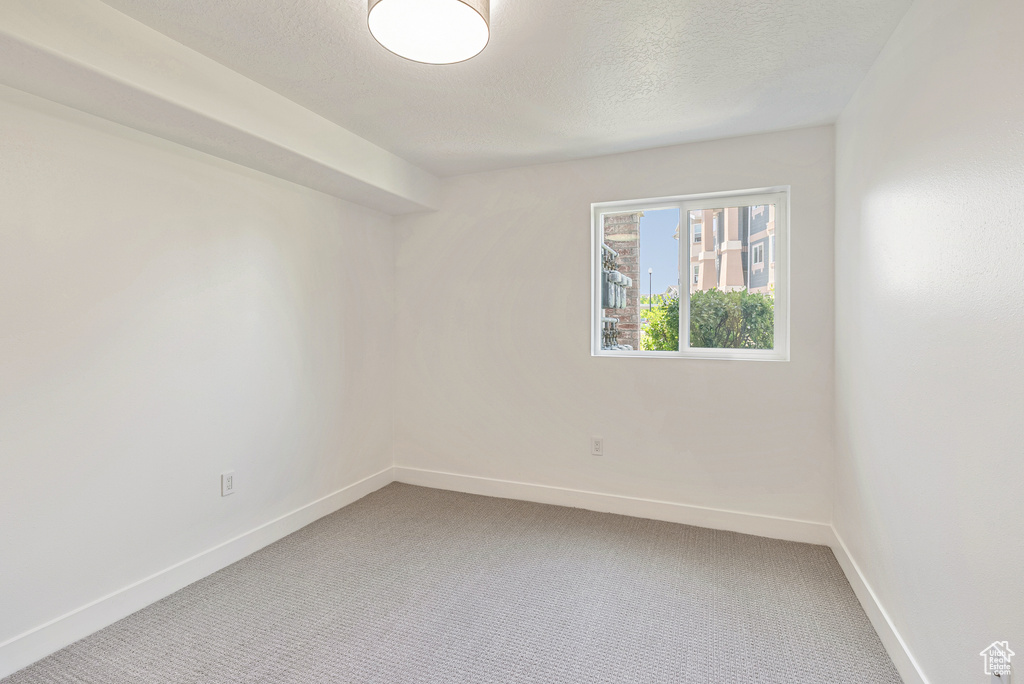 Empty room with baseboards, light colored carpet, and a textured ceiling