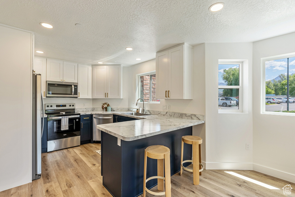 Kitchen featuring stainless steel appliances, a sink, a peninsula, light wood-type flooring, and white cabinets