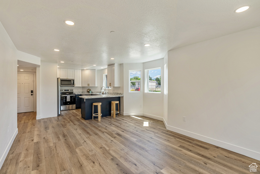 Kitchen with stainless steel appliances, recessed lighting, white cabinets, baseboards, and a kitchen breakfast bar