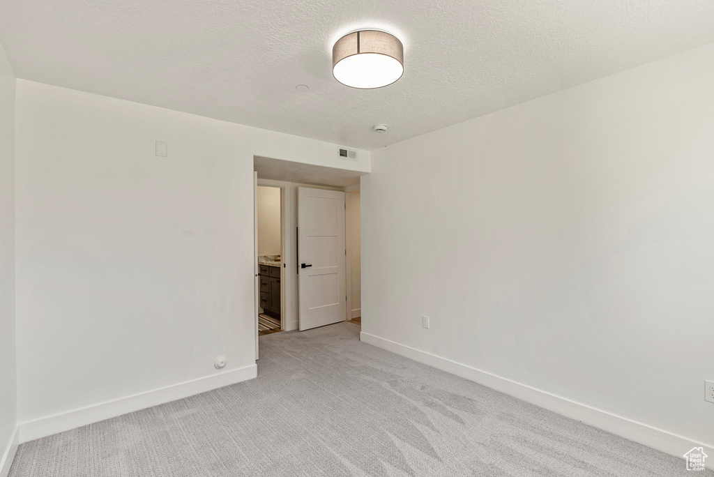 Empty room with light carpet, baseboards, and a textured ceiling