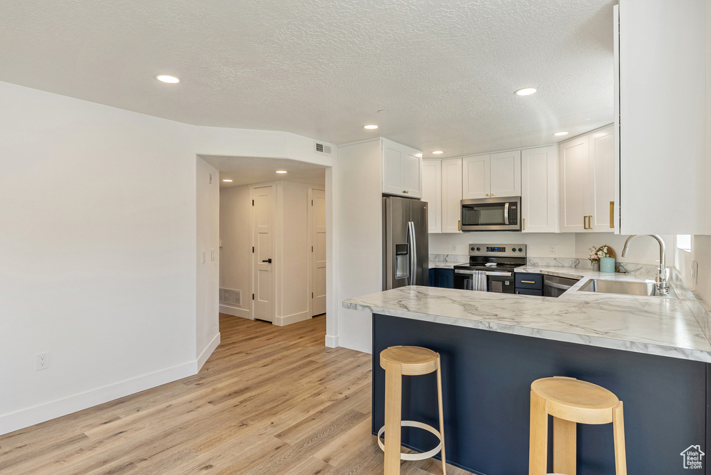 Kitchen featuring appliances with stainless steel finishes, a sink, white cabinetry, light wood-type flooring, and a peninsula