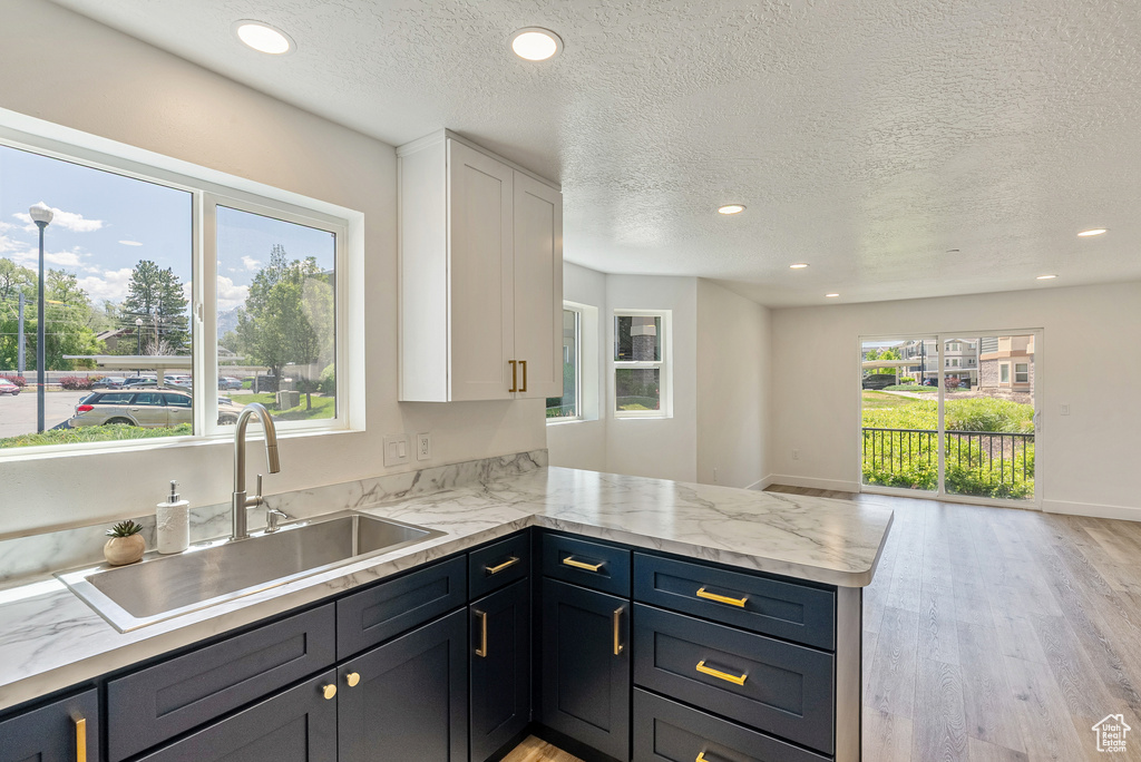 Kitchen with a sink, white cabinetry, light wood-style flooring, recessed lighting, and a peninsula