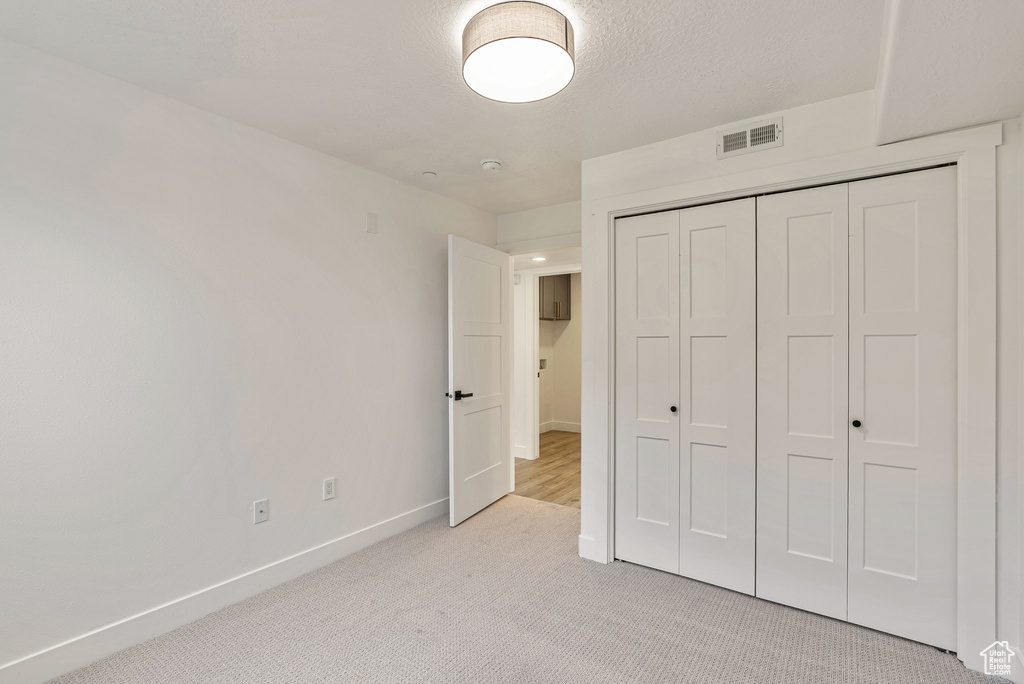 Unfurnished bedroom featuring light carpet, baseboards, and a closet