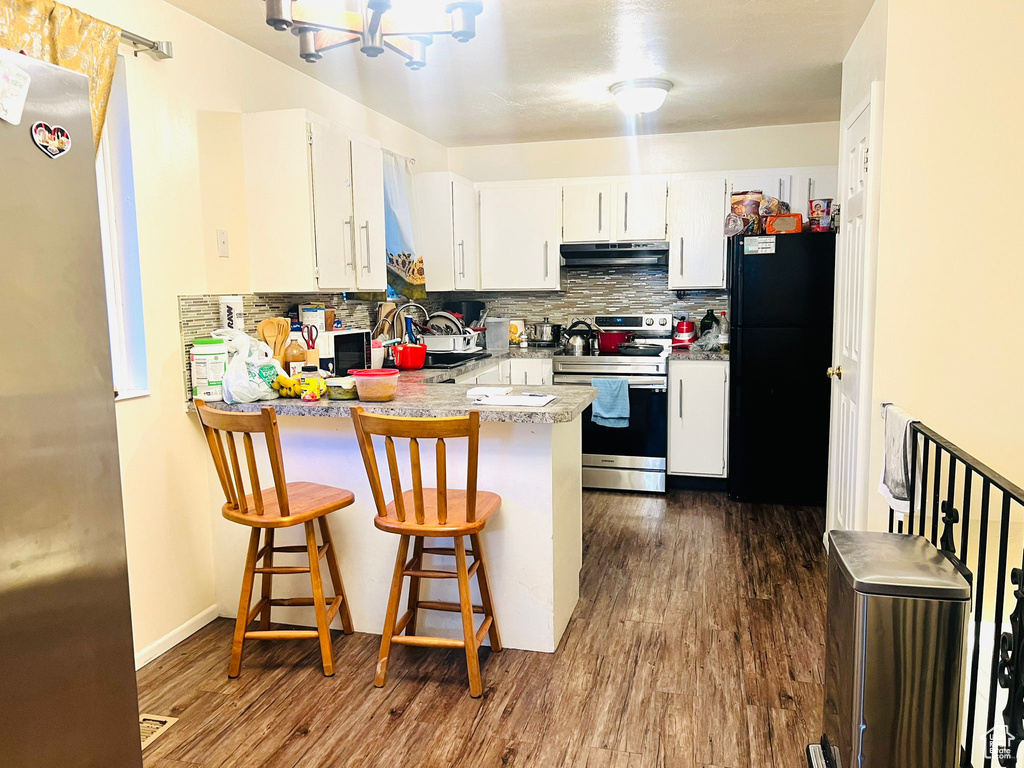 Kitchen featuring appliances with stainless steel finishes, under cabinet range hood, a peninsula, decorative backsplash, and dark wood-style flooring