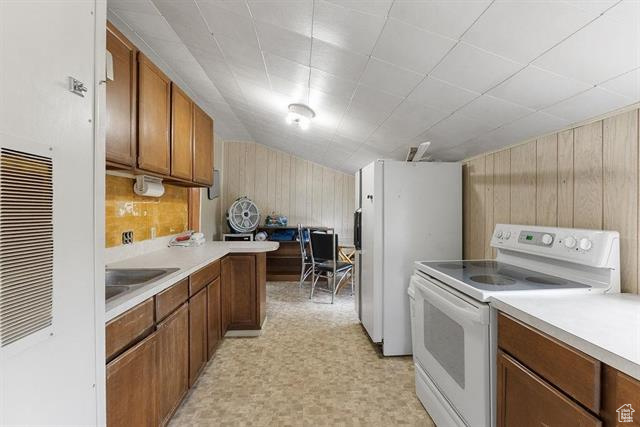 Kitchen featuring white appliances, wooden walls, light countertops, brown cabinetry, and a sink
