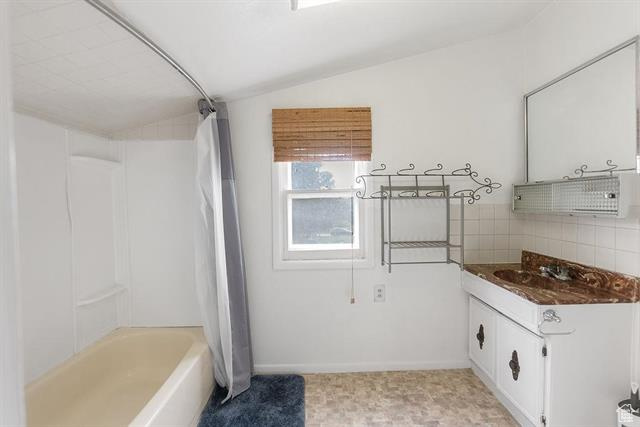 Bathroom featuring lofted ceiling, vanity, shower / tub combo with curtain, backsplash, and baseboards