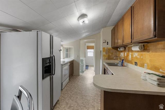 Kitchen featuring white fridge with ice dispenser, a sink, light countertops, electric range, and brown cabinets