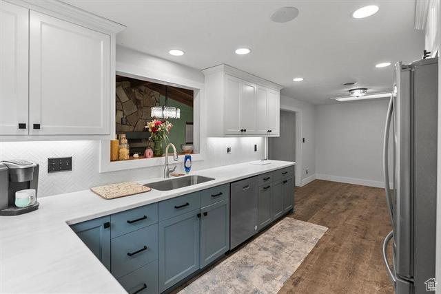 Kitchen with appliances with stainless steel finishes, a sink, white cabinets, dark wood-type flooring, and light countertops