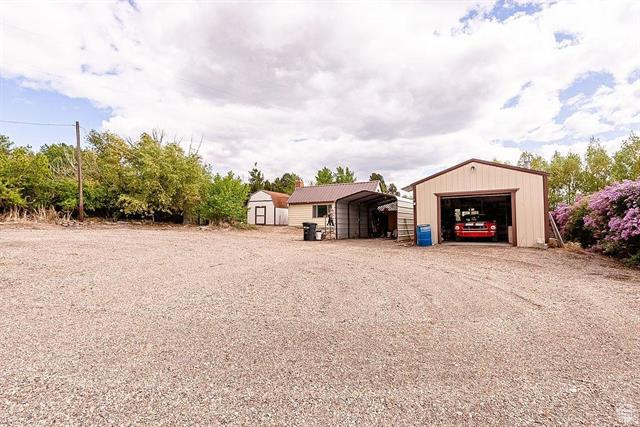 View of yard featuring dirt driveway, a carport, and a detached garage