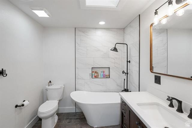 Bathroom with a freestanding bath, vanity, toilet, baseboards, and tiled shower