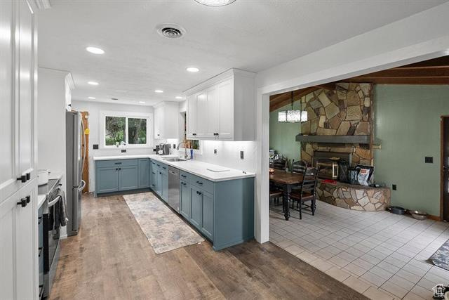 Kitchen featuring stainless steel appliances, blue cabinets, a fireplace, light countertops, and white cabinetry