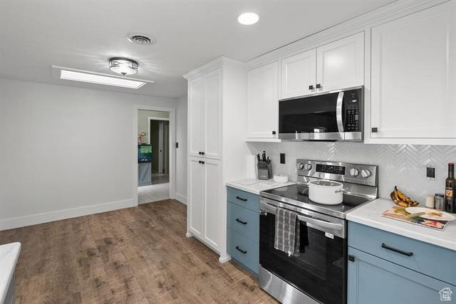 Kitchen with stainless steel appliances, light countertops, white cabinets, backsplash, and light wood-type flooring