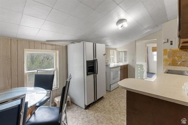 Kitchen with white appliances, a sink, light countertops, vaulted ceiling, and light floors