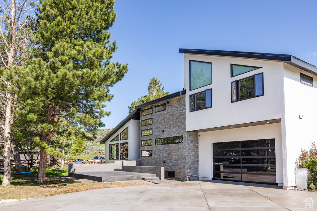 View of front of property featuring stone siding, a garage, concrete driveway, and stucco siding