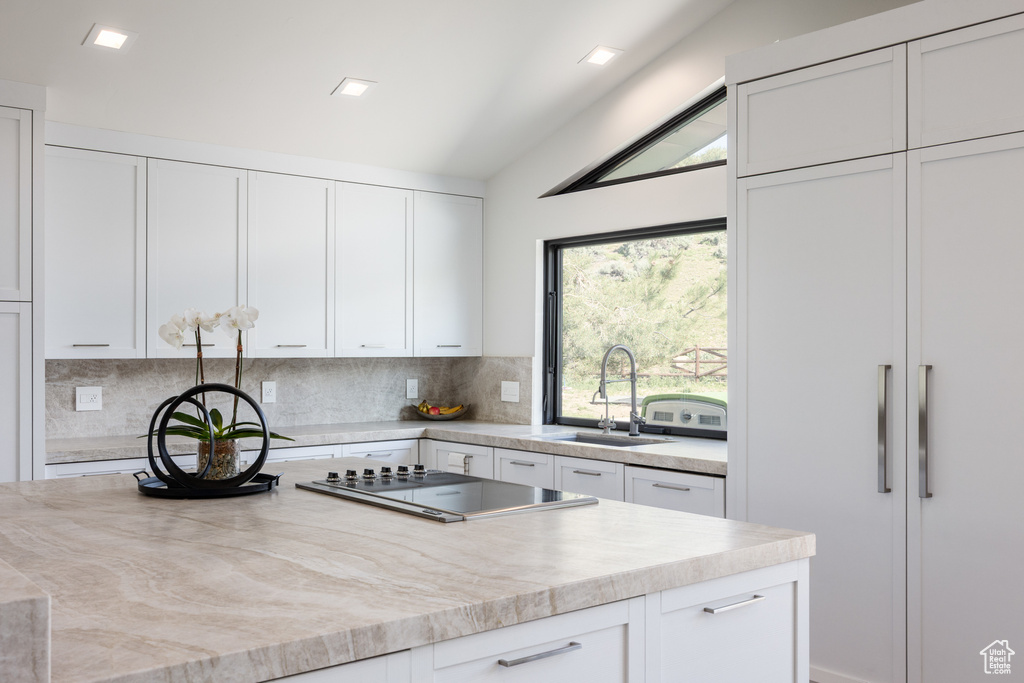 Kitchen with lofted ceiling, decorative backsplash, a sink, white cabinetry, and black electric cooktop