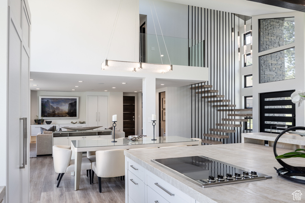 Kitchen featuring a towering ceiling, black electric cooktop, open floor plan, white cabinetry, and light wood-type flooring