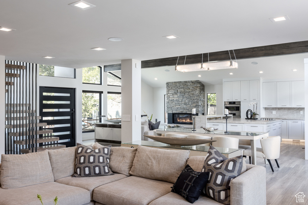 Living area with healthy amount of natural light, light wood-style flooring, beam ceiling, recessed lighting, and a stone fireplace