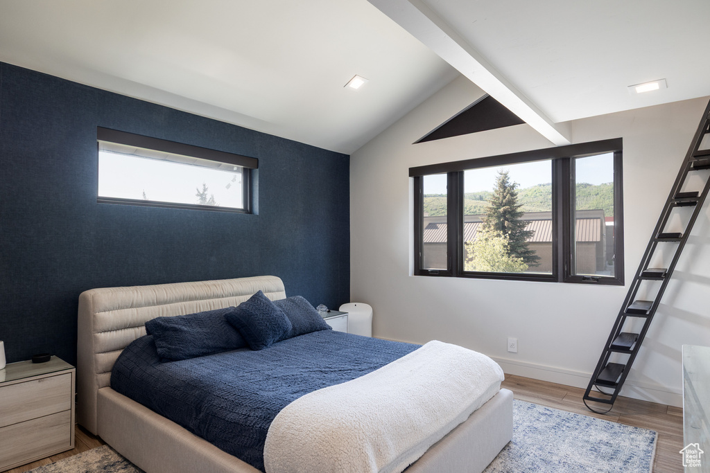 Bedroom with wood finished floors, lofted ceiling, an accent wall, and baseboards