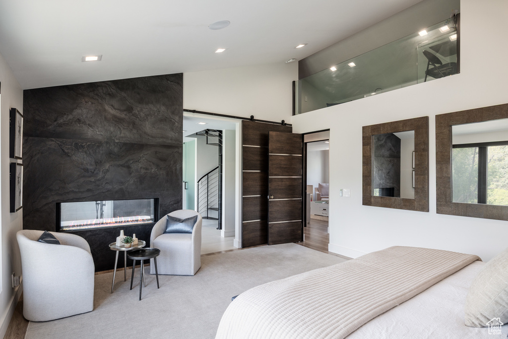 Carpeted bedroom featuring a barn door, high vaulted ceiling, recessed lighting, and a high end fireplace