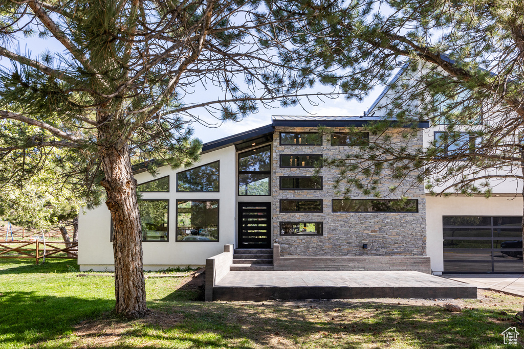 Back of house featuring stone siding, a yard, and stucco siding