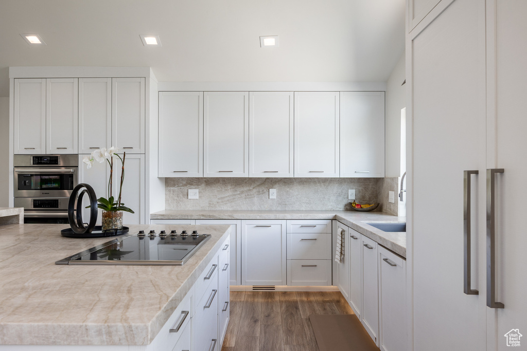 Kitchen featuring black electric cooktop, paneled refrigerator, light countertops, white cabinets, and backsplash