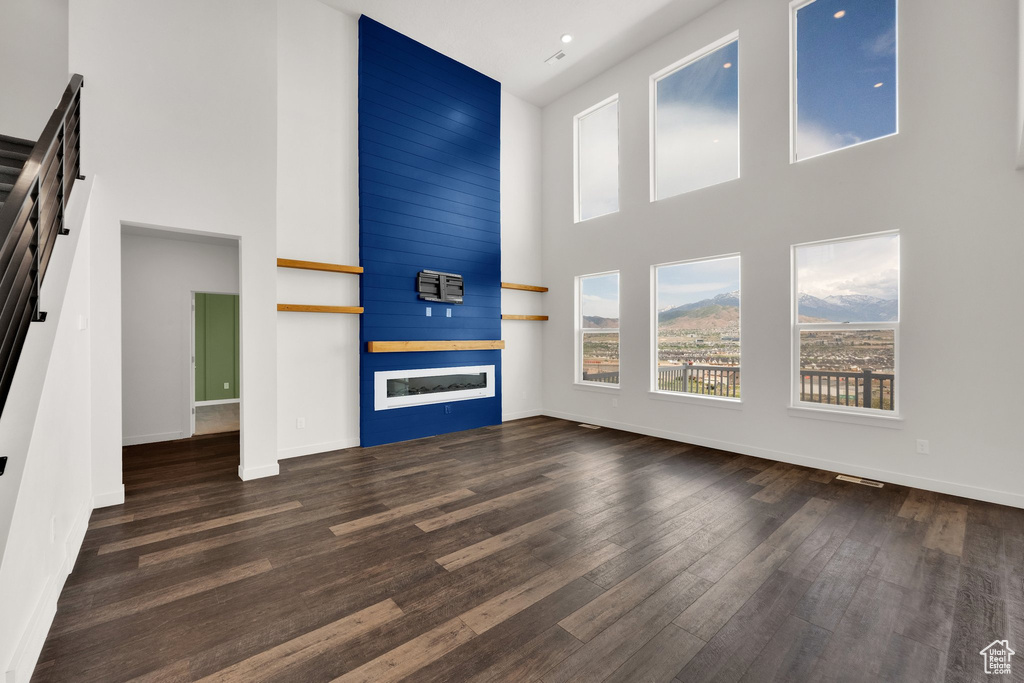 Unfurnished living room featuring a high ceiling, plenty of natural light, wood finished floors, and baseboards