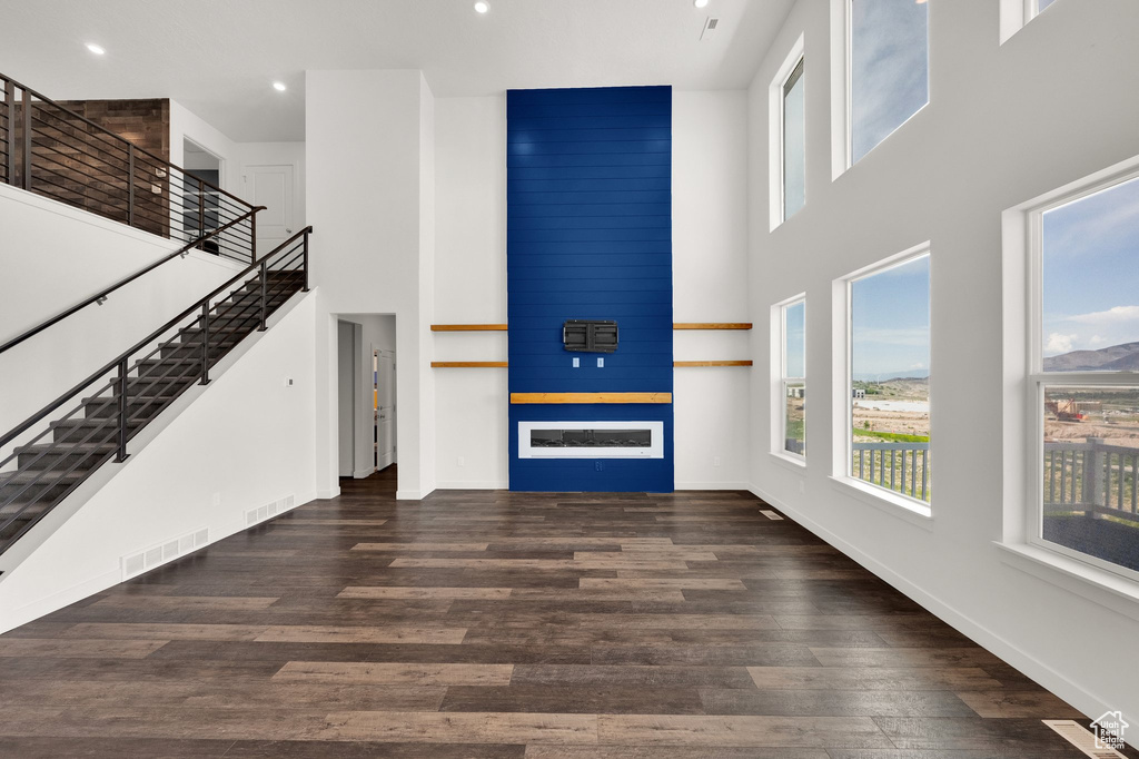 Unfurnished living room featuring a high ceiling, healthy amount of natural light, stairway, wood finished floors, and recessed lighting