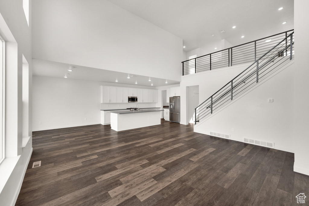 Unfurnished living room with a towering ceiling, dark wood-type flooring, recessed lighting, stairway, and baseboards