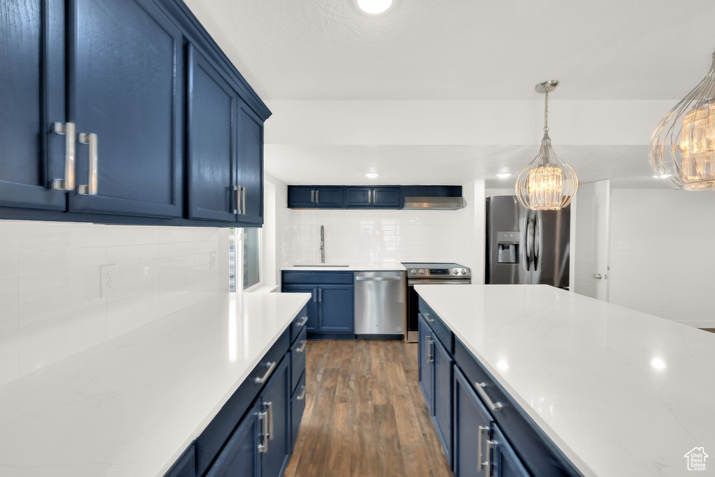 Kitchen featuring appliances with stainless steel finishes, blue cabinetry, dark wood-type flooring, and a chandelier