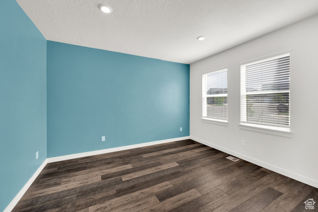 Spare room featuring dark wood-type flooring, baseboards, a textured ceiling, and recessed lighting
