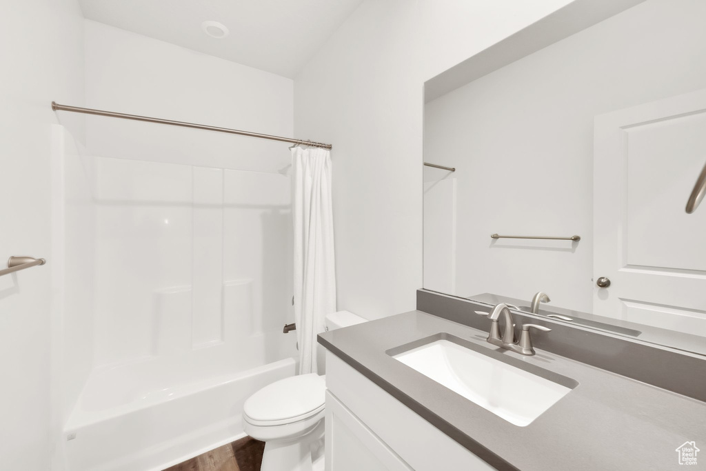 Bathroom with toilet, vanity, shower / bathtub combination with curtain, and wood finished floors