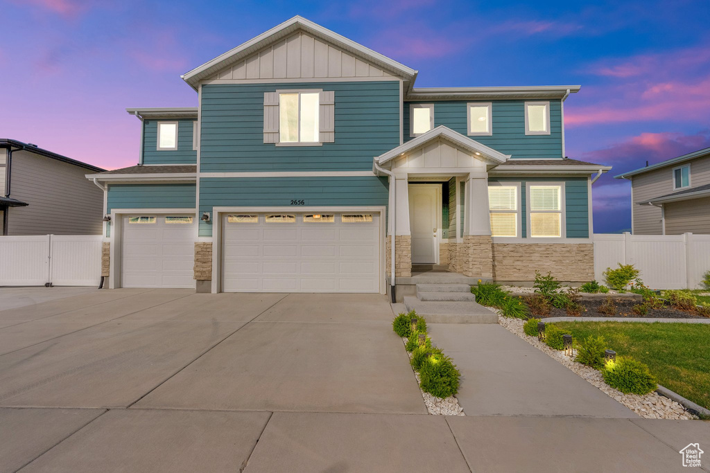 View of front facade featuring a garage, board and batten siding, driveway, and stone siding