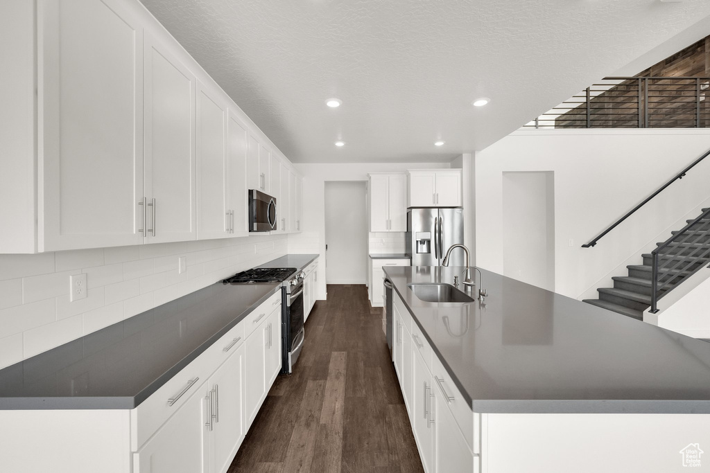 Kitchen featuring appliances with stainless steel finishes, dark countertops, a sink, dark wood finished floors, and tasteful backsplash