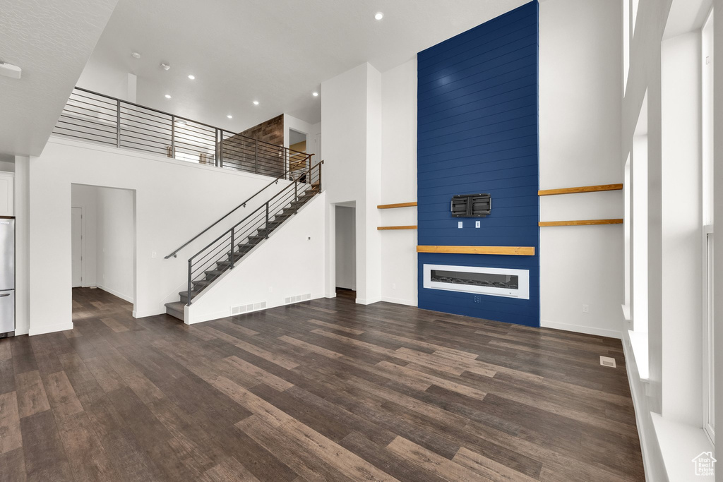 Unfurnished living room with a towering ceiling, recessed lighting, wood finished floors, stairs, and baseboards