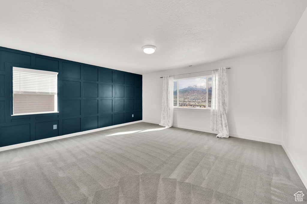 Spare room with a decorative wall, carpet flooring, baseboards, and a textured ceiling