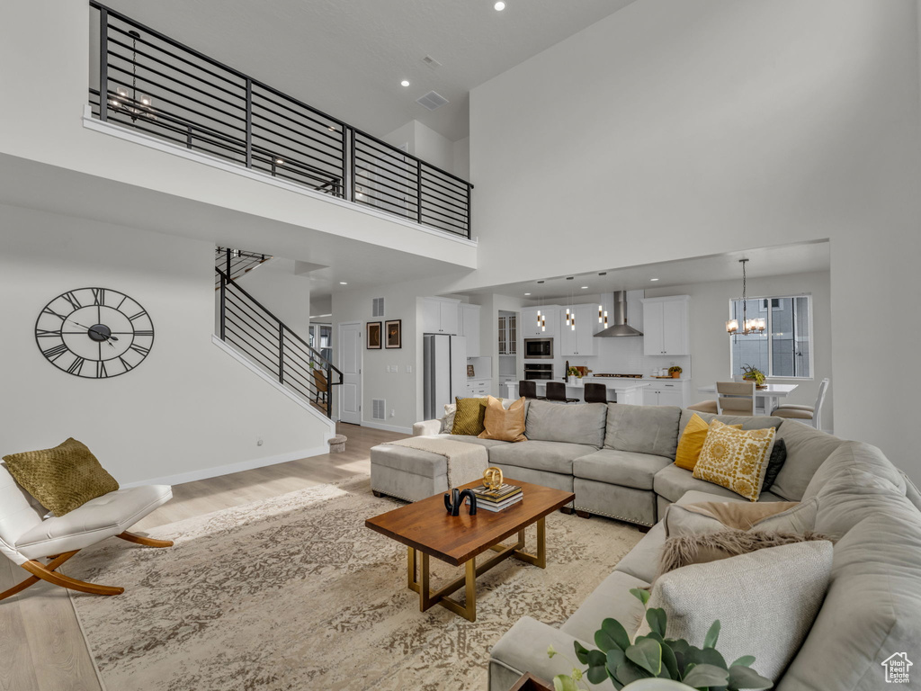 Living room featuring light wood finished floors, a towering ceiling, a chandelier, baseboards, and stairs