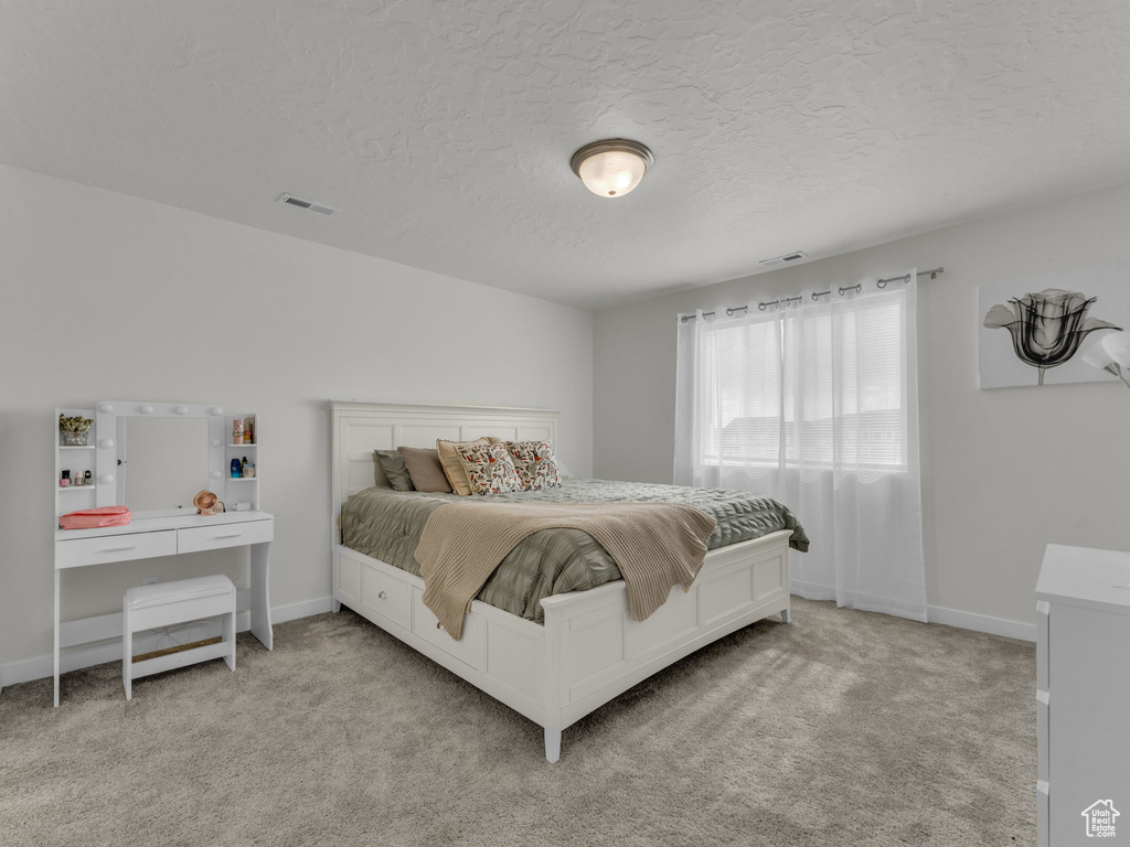 Bedroom with light carpet, a textured ceiling, and baseboards