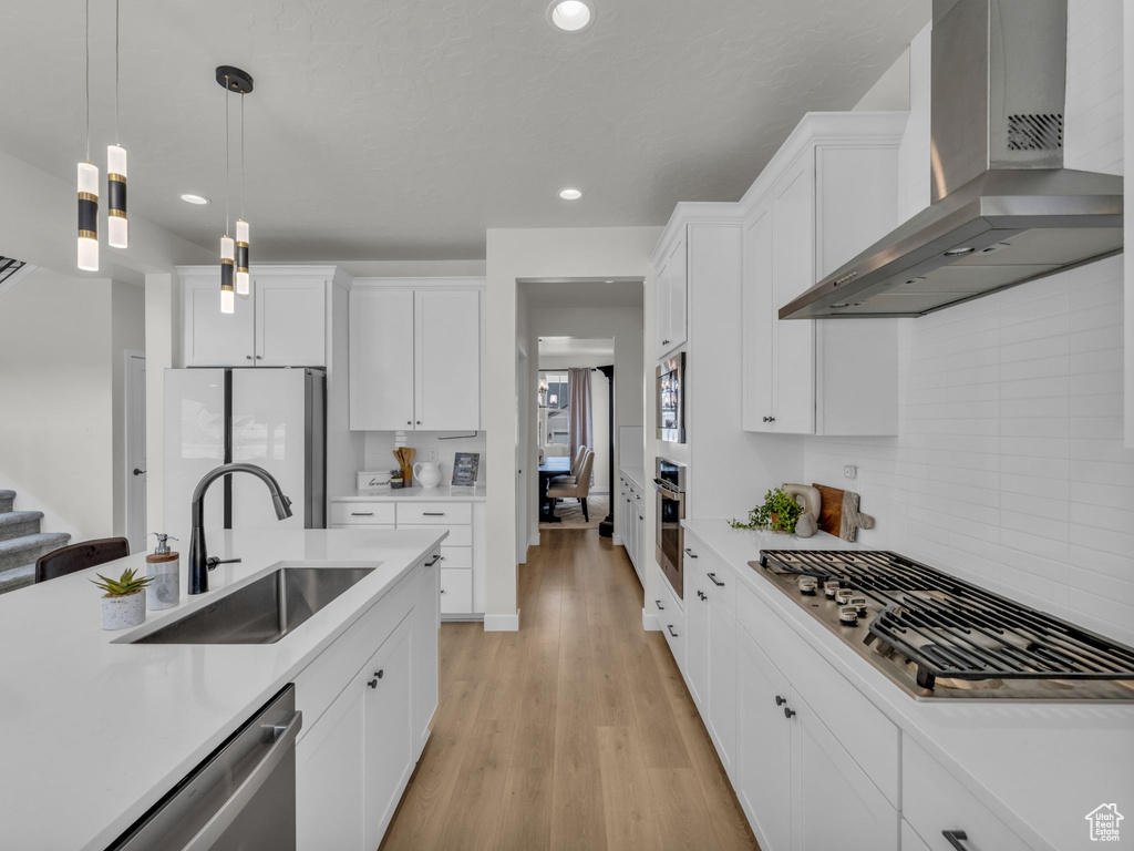 Kitchen featuring wall chimney range hood, appliances with stainless steel finishes, a sink, light countertops, and recessed lighting