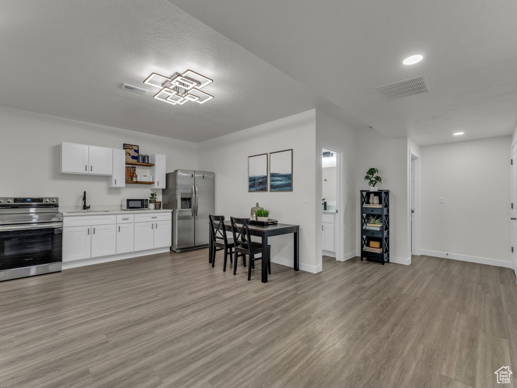 Kitchen with appliances with stainless steel finishes, a sink, light countertops, light wood-style floors, and white cabinetry