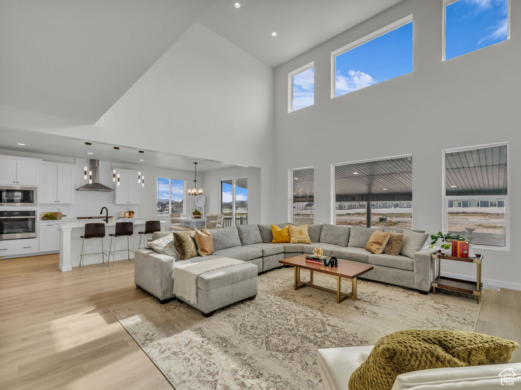 Living area with high vaulted ceiling, light wood-style flooring, recessed lighting, plenty of natural light, and a chandelier