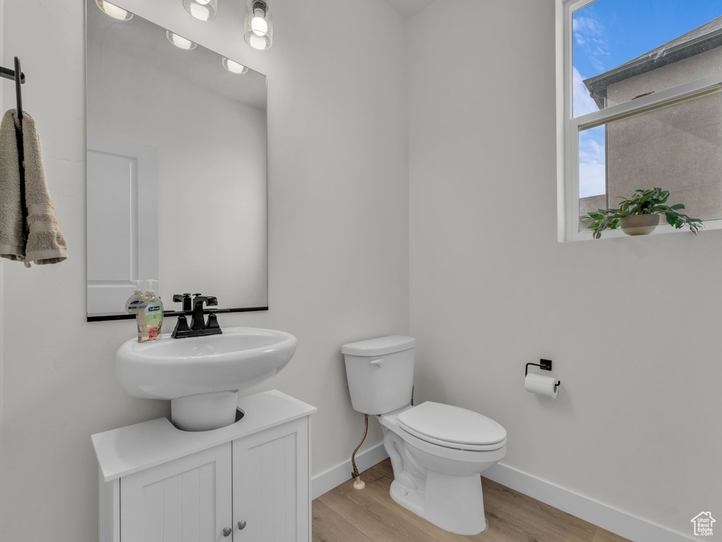 Half bathroom with baseboards, vanity, toilet, and wood finished floors
